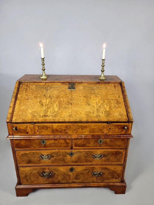 fig 4. An early 18th-century George I burr walnut bureau featuring a slant-front lid over graduating drawers with brass handles and bracket feet.