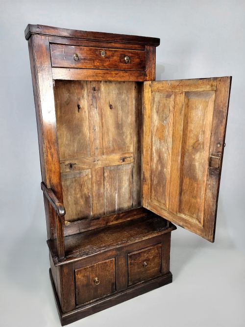 fig 2. A tall George II solid elm bacon settle featuring a high panelled cupboard back, shaped open armrests, and two integrated drawers in the base.