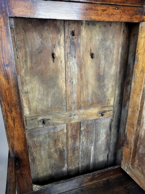 fig 3. A tall George II solid elm bacon settle featuring a high panelled cupboard back, shaped open armrests, and two integrated drawers in the base.