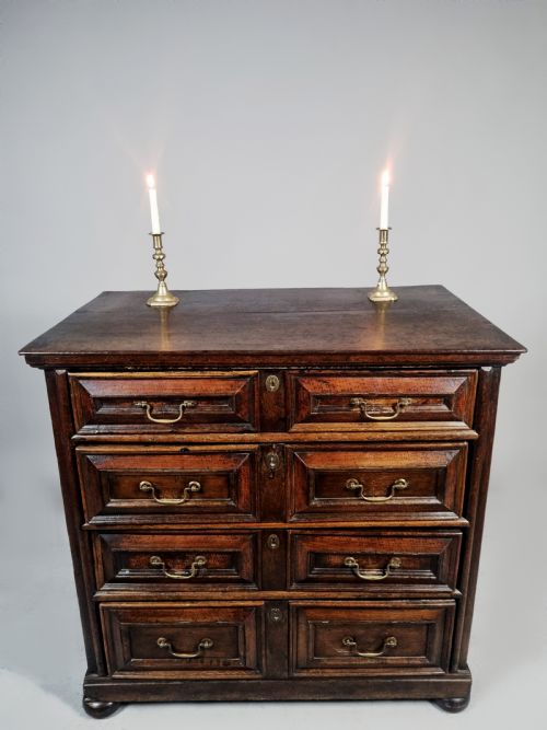 fig 2. A seventeenth-century Charles II solid oak chest of drawers featuring geometric panelled drawer fronts, brass drop handles, and bun feet.