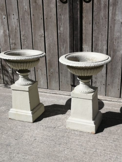 fig 2. A pair of off-white painted cast iron garden urns featuring fluted rims and bodies set upon square plinths.