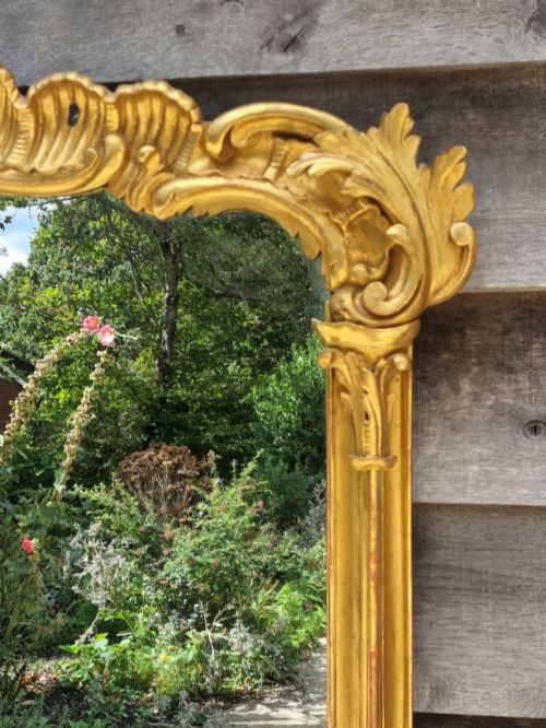 fig 2. A large 19th-century giltwood mirror featuring carved C-scroll cresting, acanthus leaf detailing, and a gilded frame surrounding a glass plate.