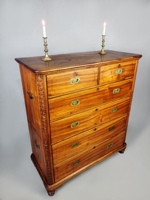 fig 1. A nineteenth-century teak campaign chest of drawers featuring flush brass handles, keyholes, two short over three long drawers, and carved side pilasters.