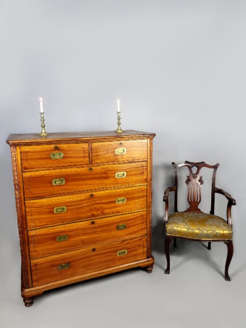 fig 2. A nineteenth-century teak campaign chest of drawers featuring flush brass handles, keyholes, two short over three long drawers, and carved side pilasters.