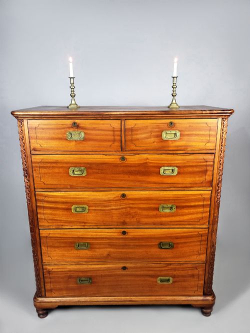fig 3. A nineteenth-century teak campaign chest of drawers featuring flush brass handles, keyholes, two short over three long drawers, and carved side pilasters.