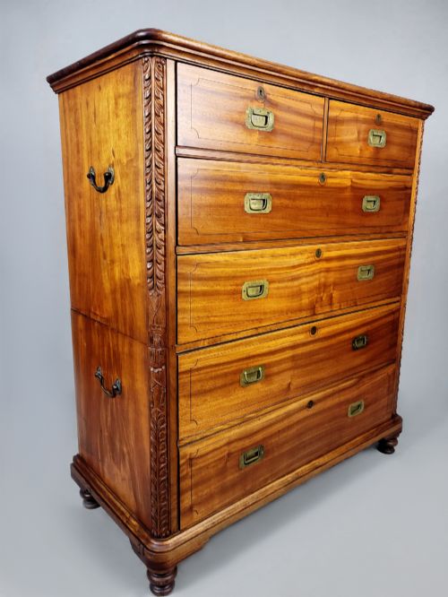 fig 4. A nineteenth-century teak campaign chest of drawers featuring flush brass handles, keyholes, two short over three long drawers, and carved side pilasters.