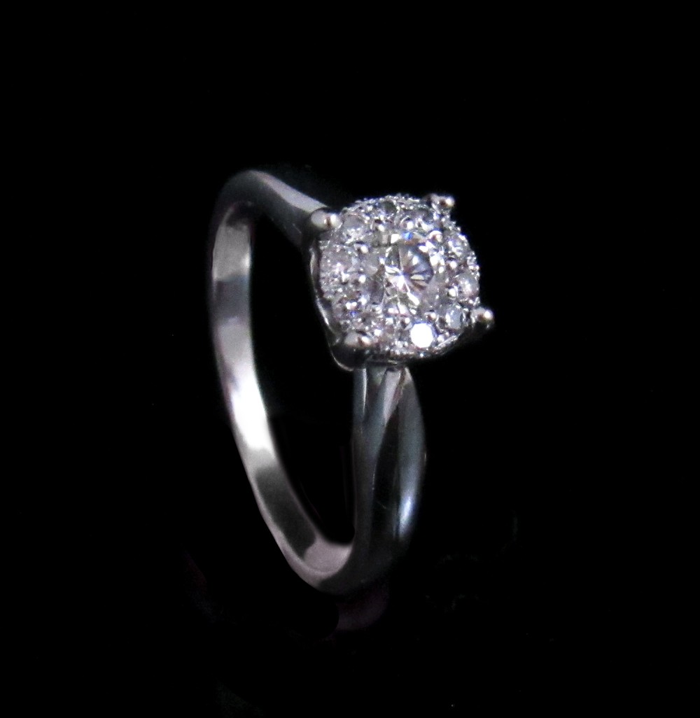 An 18kt white gold ring featuring a raised round cluster setting set with multiple brilliant-cut diamonds.