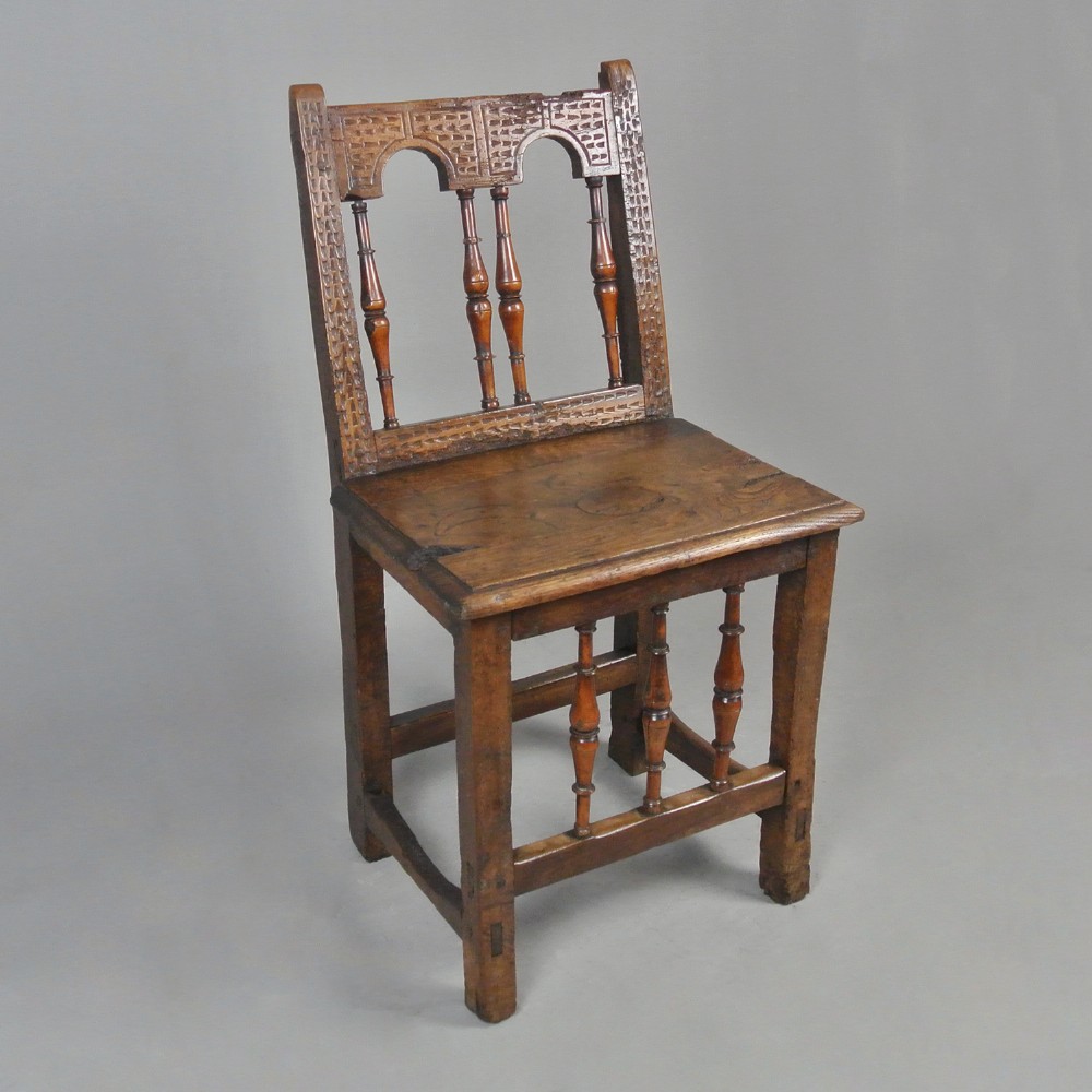 A 17th-century carved walnut and yew back stool chair featuring arcaded back panels and turned spindles.