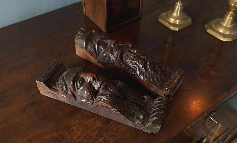 A pair of 17th-century hand-carved dark oak timber corbels depicting bearded male faces.