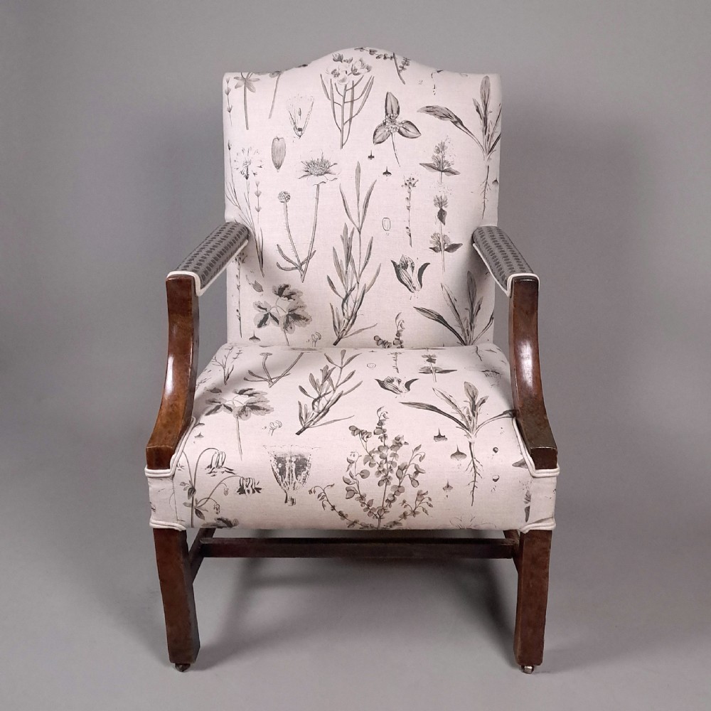 A George III yew wood Gainsborough armchair featuring monochrome botanical fabric upholstery, padded armrests, square legs, and brass castors.