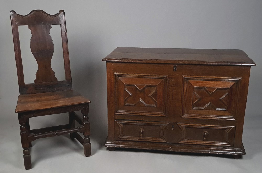 A 17th-century dark oak mule chest featuring geometric carved panel fronts, a lower drawer with brass drop handles, and a flat hinged top. View III
