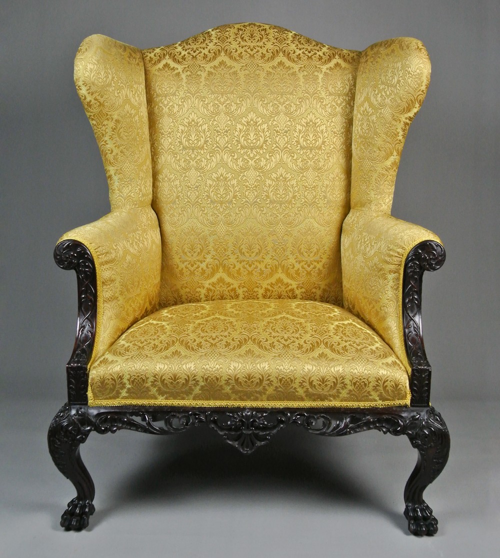 A Georgian mahogany wingback armchair upholstered in patterned gold damask fabric, featuring carved cabriole legs and an ornate apron.