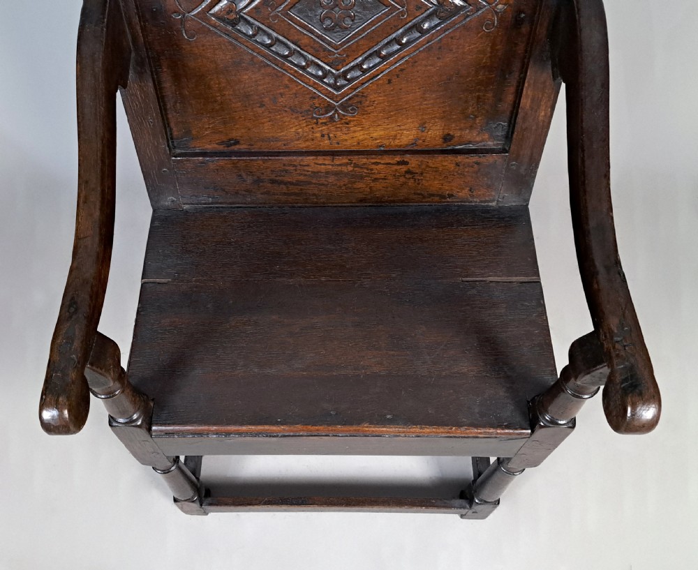 A 17th-century dark oak wainscot armchair featuring a carved lozenge back panel, shaped cresting rail, curved armrests, and turned legs. View IV