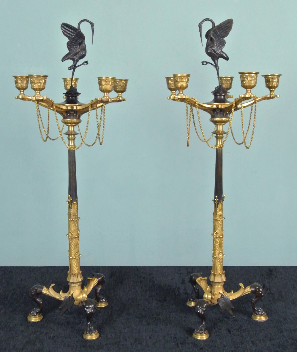 A pair of tall nineteenth-century dark bronze and gilded ormolu candelabra featuring crane finials, hanging chains, multi-nozzle arms, and tripod claw bases.