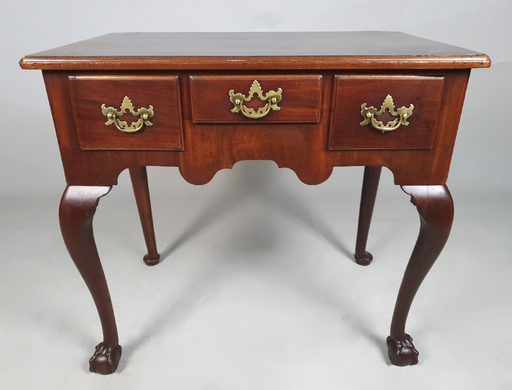 An 18th-century George III red walnut lowboy table with three brass-handled drawers, a shaped apron, and front cabriole legs ending in carved ball-and-claw feet.