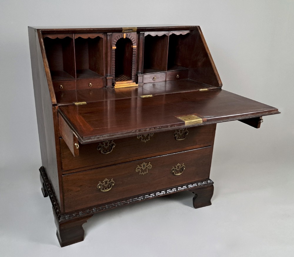 An eighteenth-century Chippendale style dark padauk wood writing bureau featuring an open fall-front writing surface, architectural pigeonhole section, brass handles, and bracket feet.