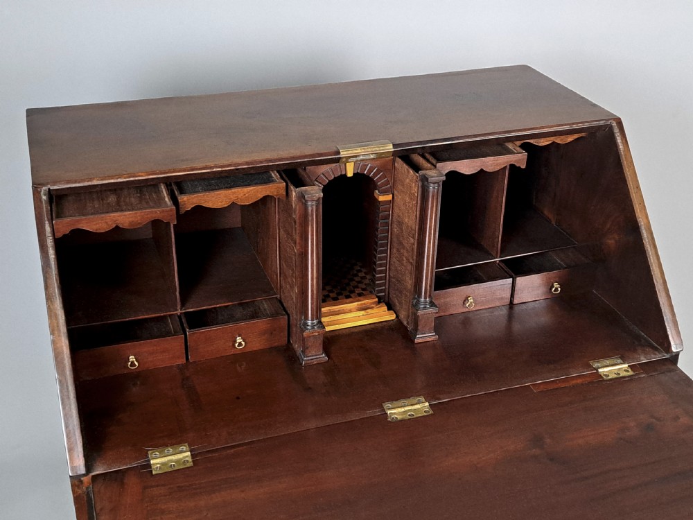 An eighteenth-century Chippendale style dark padauk wood writing bureau featuring an open fall-front writing surface, architectural pigeonhole section, brass handles, and bracket feet. View IV