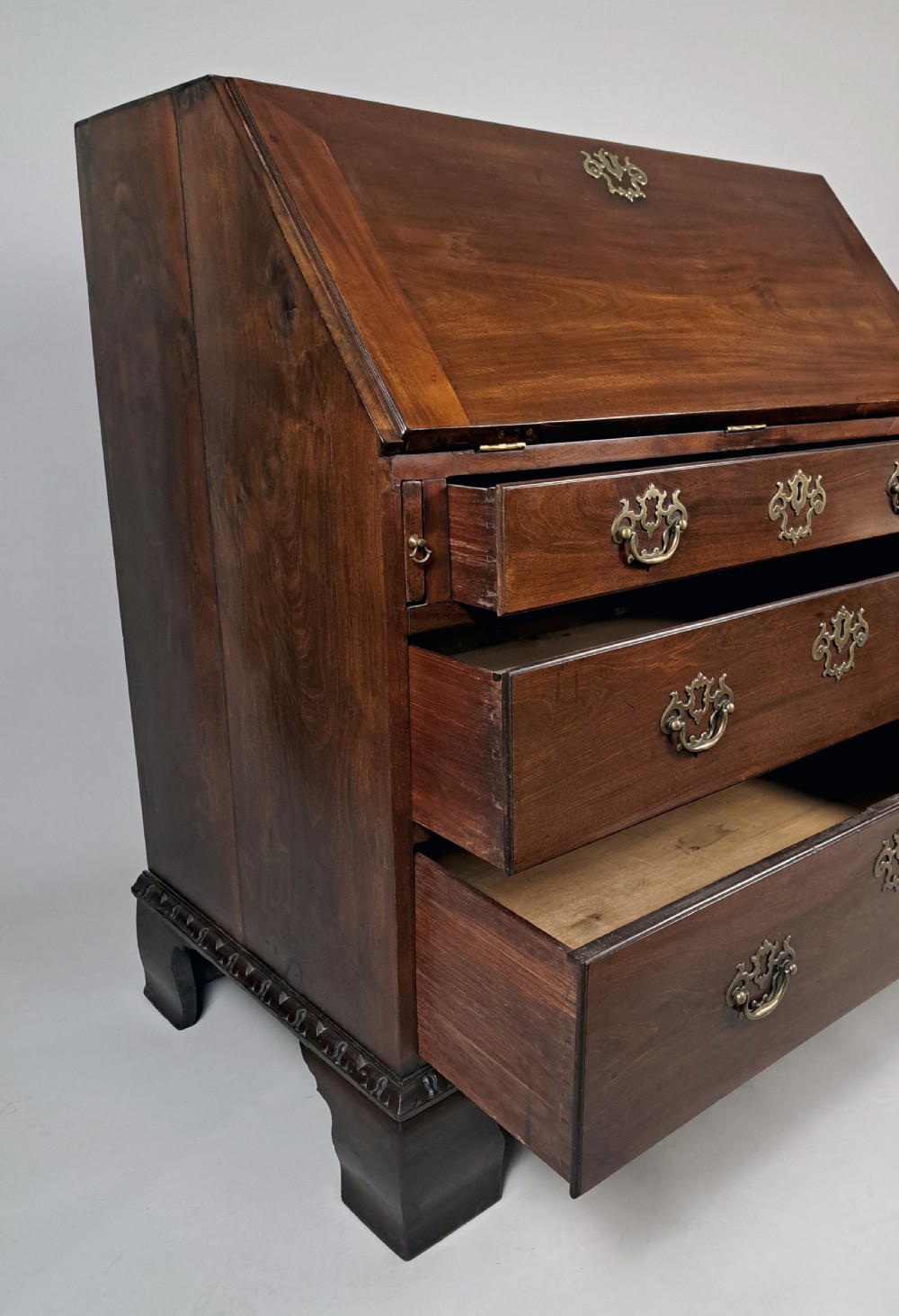 An eighteenth-century Chippendale style dark padauk wood writing bureau featuring an open fall-front writing surface, architectural pigeonhole section, brass handles, and bracket feet. View VIII