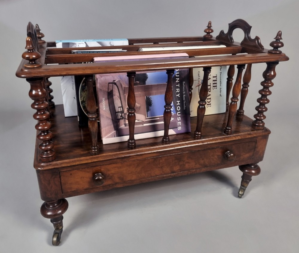 A Victorian walnut music Canterbury featuring turned spindles, division compartments, a lower drawer with twin knobs, and turned legs with brass castors.