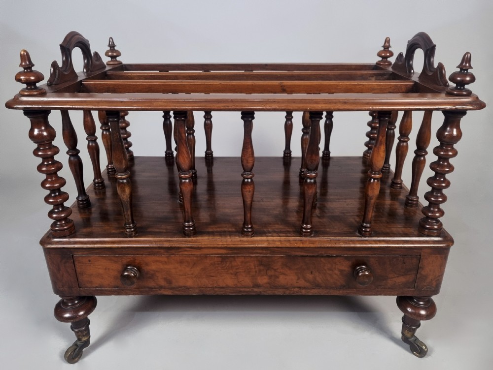 A Victorian walnut music Canterbury featuring turned spindles, division compartments, a lower drawer with twin knobs, and turned legs with brass castors. View III