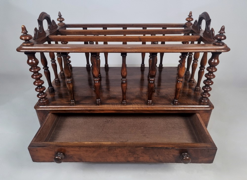 A Victorian walnut music Canterbury featuring turned spindles, division compartments, a lower drawer with twin knobs, and turned legs with brass castors. View IV