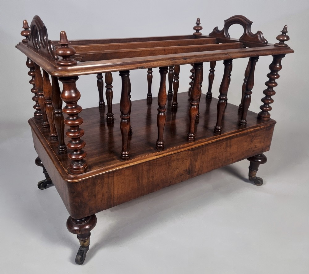 A Victorian walnut music Canterbury featuring turned spindles, division compartments, a lower drawer with twin knobs, and turned legs with brass castors. View VI