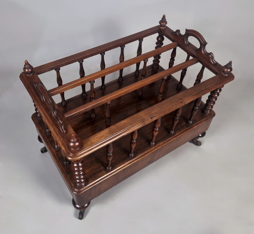 A Victorian walnut music Canterbury featuring turned spindles, division compartments, a lower drawer with twin knobs, and turned legs with brass castors. View VII