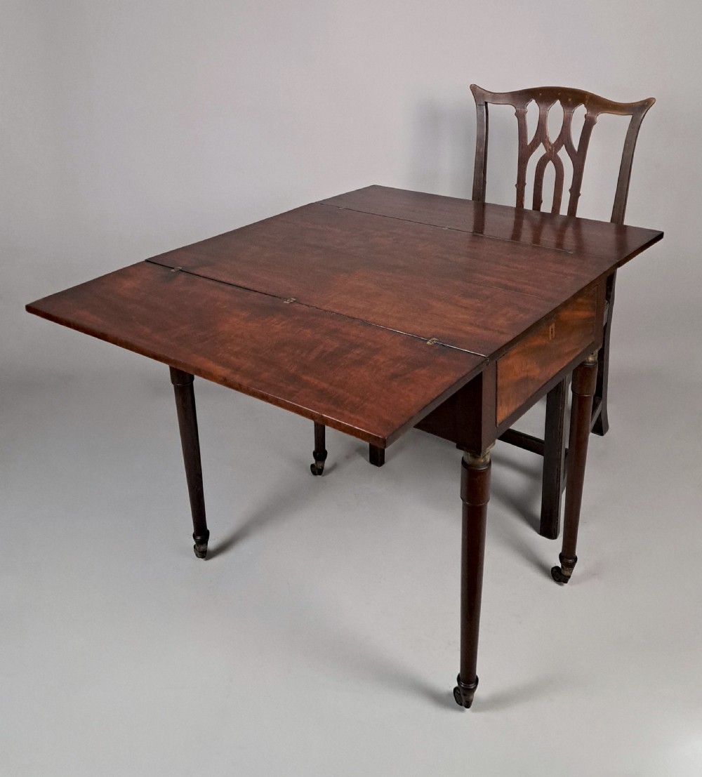 A George III mahogany campaign table with a split hinged top, flame mahogany drawer front, brass collar mounts, turned tapering legs, and brass castors. View II
