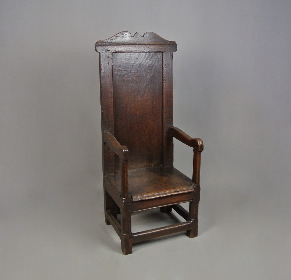 A 17th-century Jacobean dark oak wainscot armchair featuring a high panelled back, straight arms, and heavy square legs joined by stretchers.