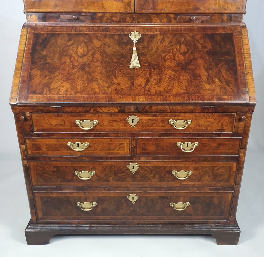 An early 18th-century Queen Anne burr walnut bureau cabinet featuring a double-domed pediment, open doors revealing multiple pigeonholes, a sloped drop-front writing desk, and lower storage drawers. View IV