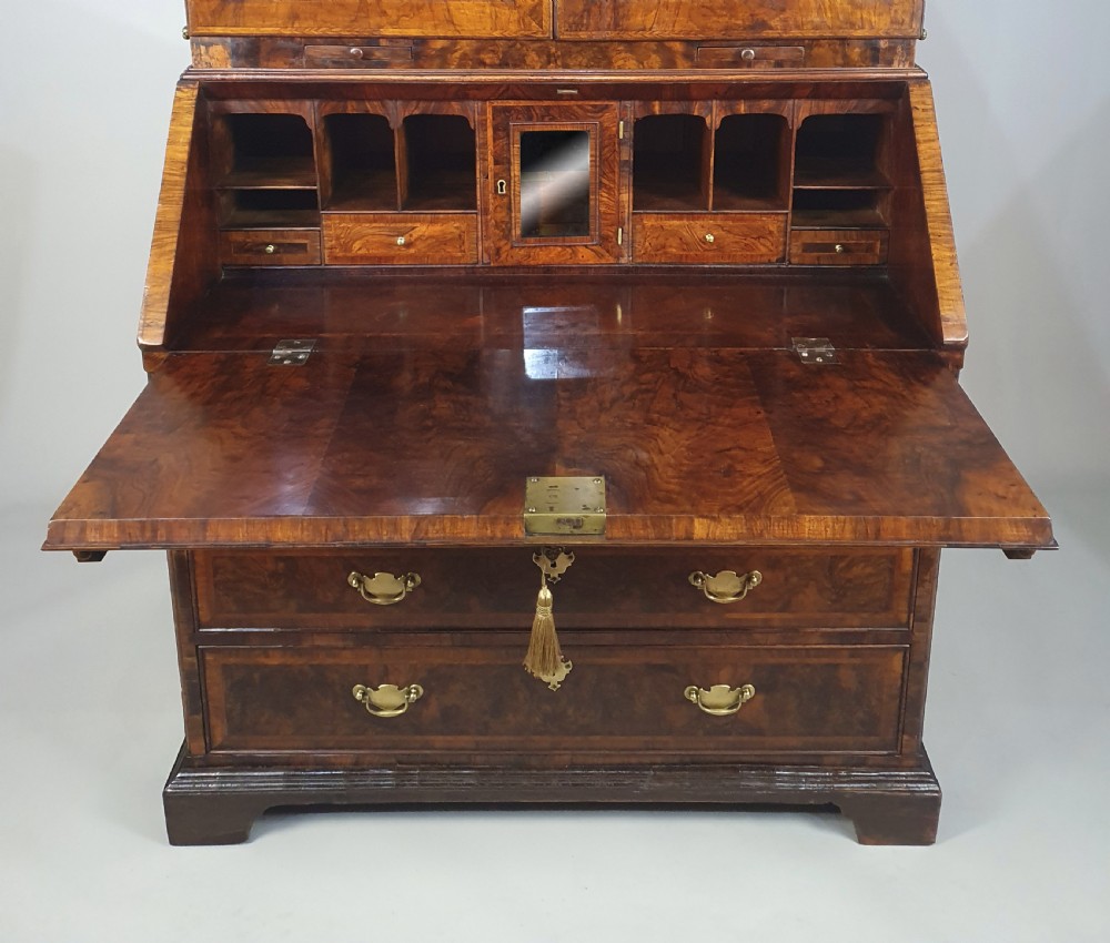 An early 18th-century Queen Anne burr walnut bureau cabinet featuring a double-domed pediment, open doors revealing multiple pigeonholes, a sloped drop-front writing desk, and lower storage drawers. View V