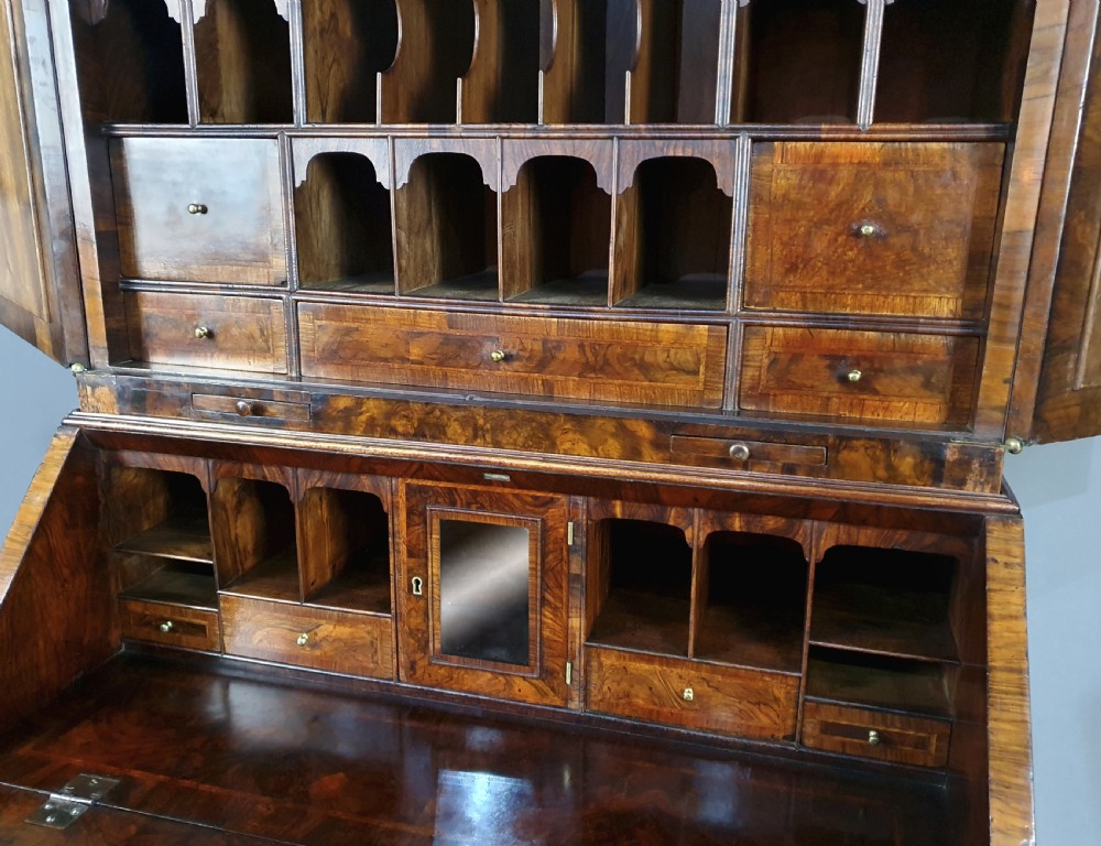 An early 18th-century Queen Anne burr walnut bureau cabinet featuring a double-domed pediment, open doors revealing multiple pigeonholes, a sloped drop-front writing desk, and lower storage drawers. View VI