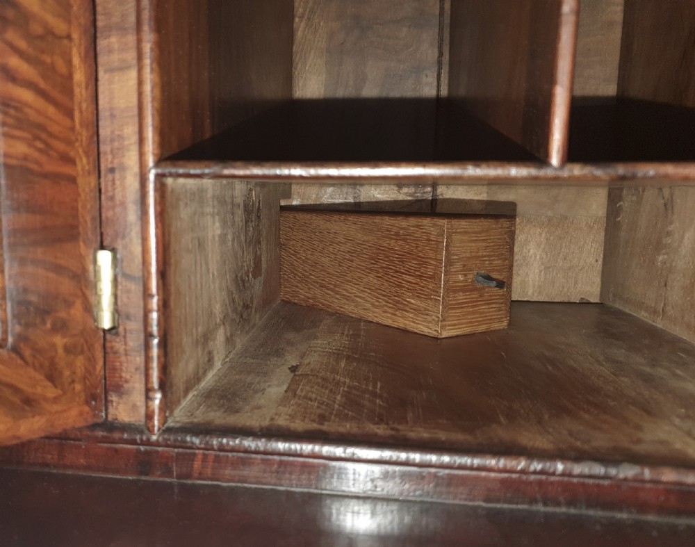 An early 18th-century Queen Anne burr walnut bureau cabinet featuring a double-domed pediment, open doors revealing multiple pigeonholes, a sloped drop-front writing desk, and lower storage drawers. View VIII