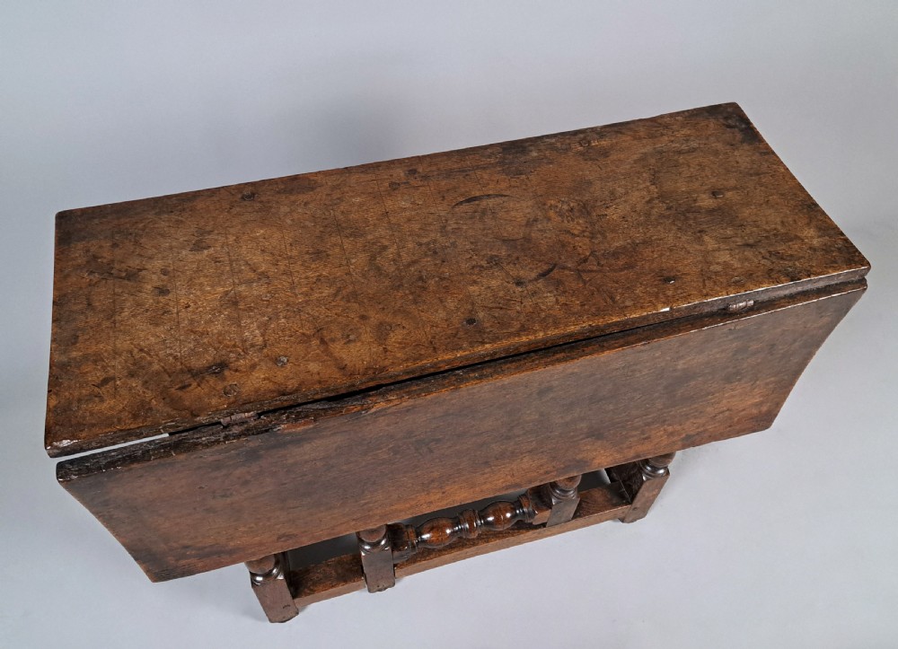 A 17th-century Charles II dark oak drop-leaf side table featuring turned legs, a hinged top flap, and sturdy lower stretchers. View III