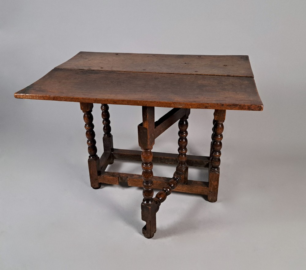 A 17th-century Charles II dark oak drop-leaf side table featuring turned legs, a hinged top flap, and sturdy lower stretchers. View IV