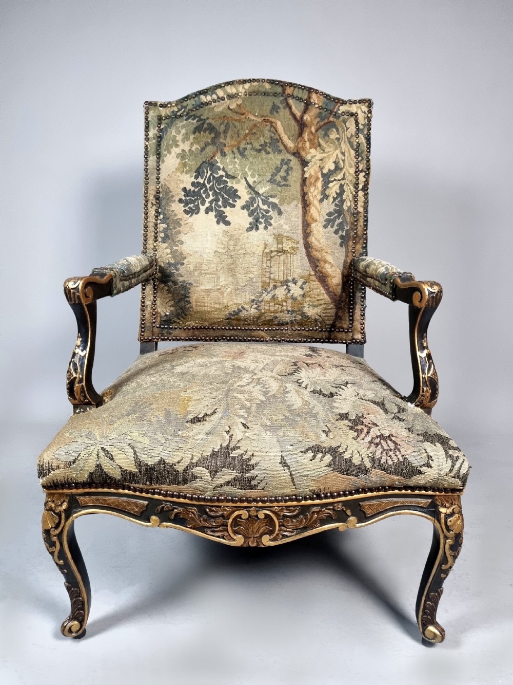 A George III Gainsborough armchair with carved cabriole legs, parcel gilding, and green landscape tapestry upholstery trimmed with brass studs.