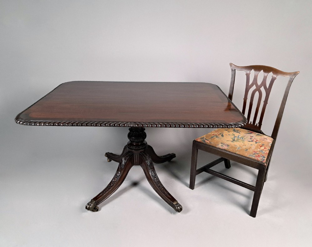 A George III mahogany dining table featuring a rectangular top with carved rope-twist edging, resting on a turned central column and four carved legs with brass castors. View VI