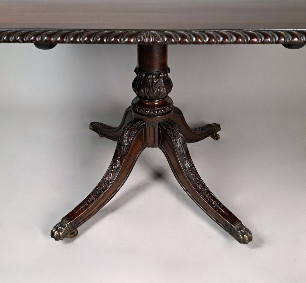 A George III mahogany dining table featuring a rectangular top with carved rope-twist edging, resting on a turned central column and four carved legs with brass castors. View VII