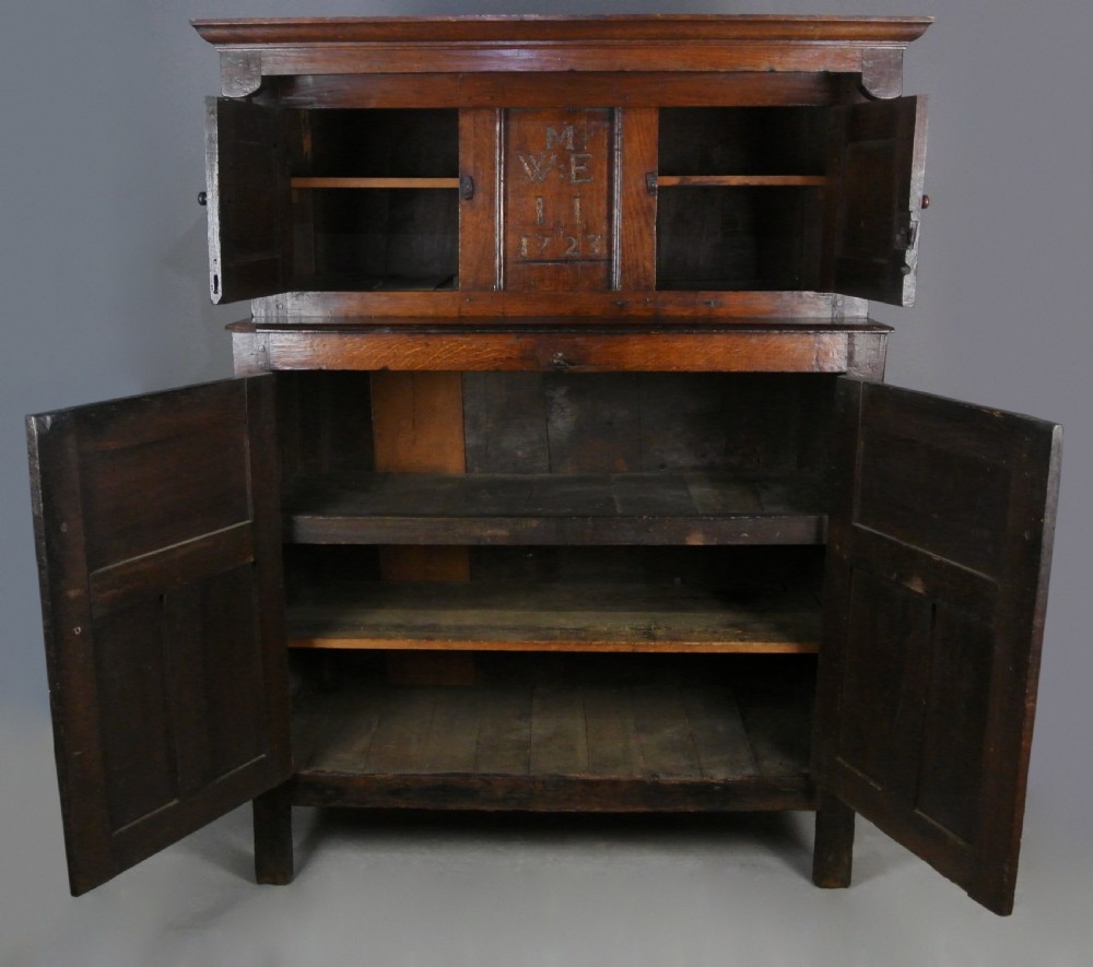 An 18th-century English dark oak court cupboard featuring carved initials, the date 1723, panelled doors, drop pendants, and iron hinges. View V