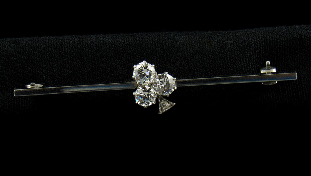 An Art Deco 18ct white gold bar brooch featuring a central trefoil cluster of old-cut diamonds on a slender horizontal bar.