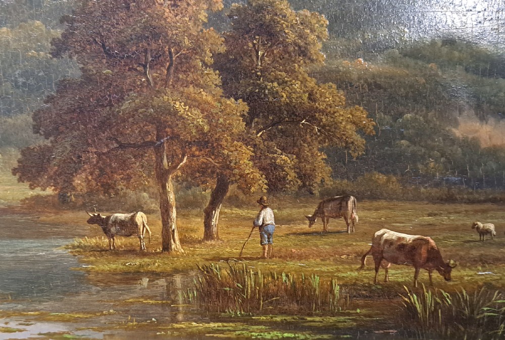 An early 19th-century English oil on board landscape painting depicting a pastoral river scene with cattle and castle ruins, housed within an ornate gold giltwood frame. View VI