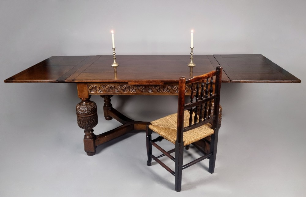 A carved warm brown oak extending dining table featuring heavy bulbous cup-and-cover legs, carved frieze detailing, and a floor stretcher base. View III