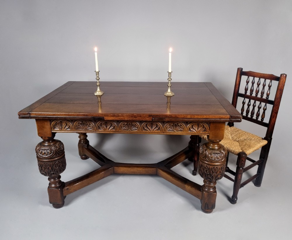 A carved warm brown oak extending dining table featuring heavy bulbous cup-and-cover legs, carved frieze detailing, and a floor stretcher base. View IV