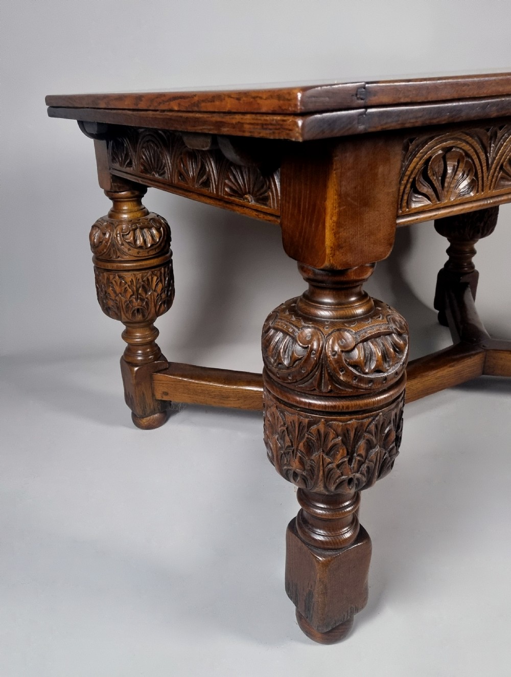 A carved warm brown oak extending dining table featuring heavy bulbous cup-and-cover legs, carved frieze detailing, and a floor stretcher base. View V