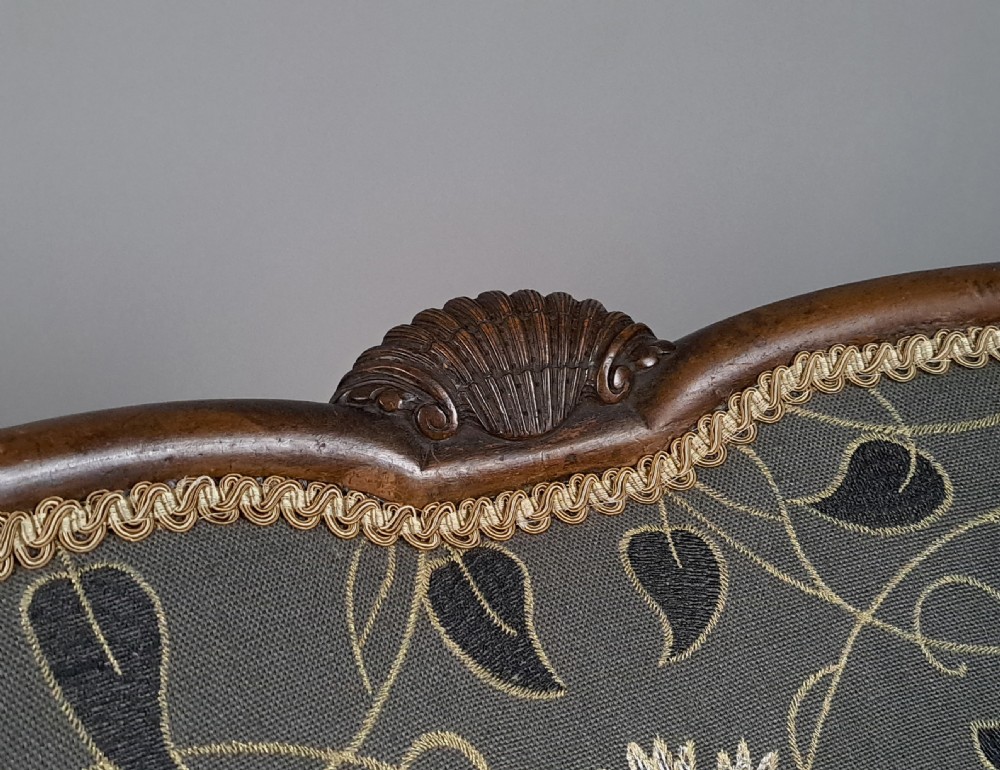 A 19th-century Queen Anne revival armchair featuring patterned grey floral upholstery, curved wings, shell carved top crest, and cabriole timber legs. View V