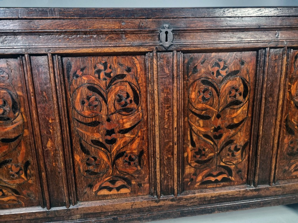 A 17th-century dark oak chest featuring four front panels with intricate floral marquetry inlay, a panelled top, and an iron keyhole. View II
