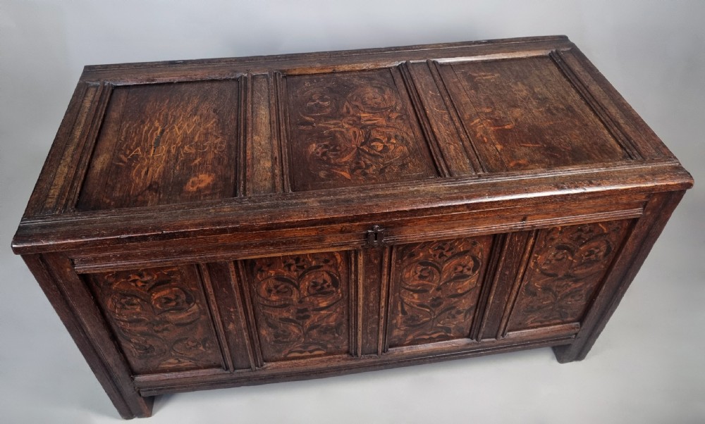 A 17th-century dark oak chest featuring four front panels with intricate floral marquetry inlay, a panelled top, and an iron keyhole. View V