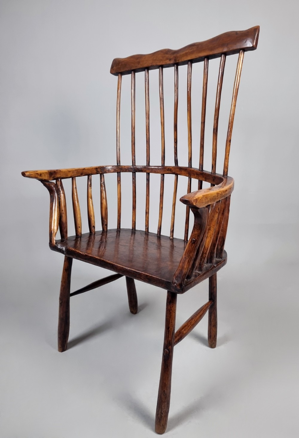 A primitive 18th-century Welsh stick armchair made from dark polished wood featuring a comb back, tapered stick spindles, and an organic curved frame. View V