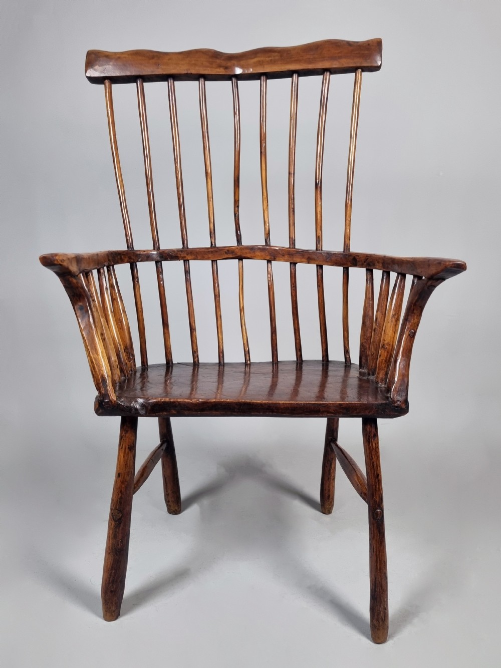 A primitive 18th-century Welsh stick armchair made from dark polished wood featuring a comb back, tapered stick spindles, and an organic curved frame. View VI