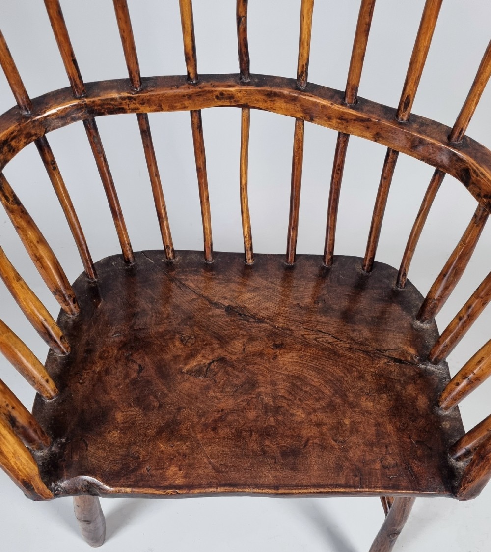 A primitive 18th-century Welsh stick armchair made from dark polished wood featuring a comb back, tapered stick spindles, and an organic curved frame. View VII